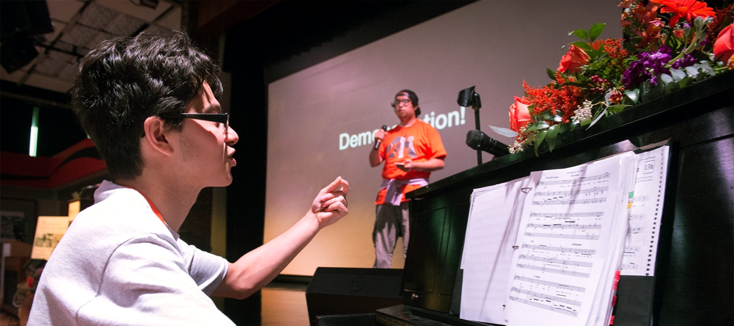 Lucas Colon at the piano directing a student on stage