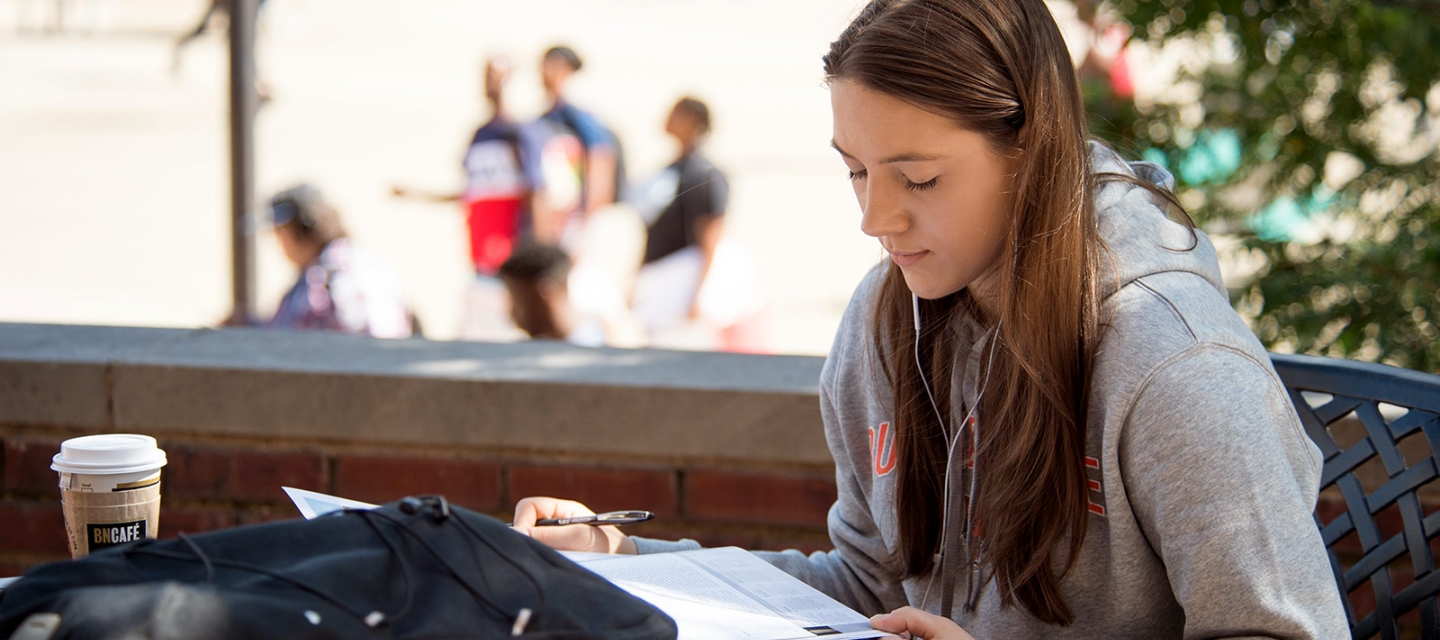 Student with textbook at a table in the quad